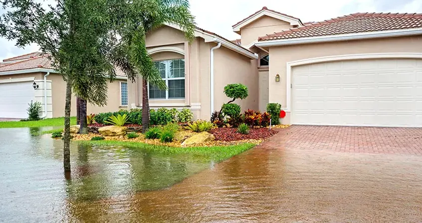 Floodwater covering a driveway and lawn outside a stucco house